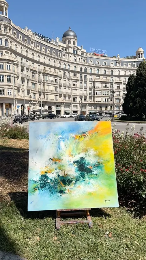 Tableau abstrait jaune, vert et turquoise de Régine Gardan, sur un chevalet dans un jardin, devant un grand immeuble ancien