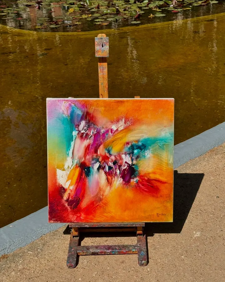 Tableau abstrait orange, turquoise et magenta de Régine Gardan, sur un chevalet au bord d'un bassin