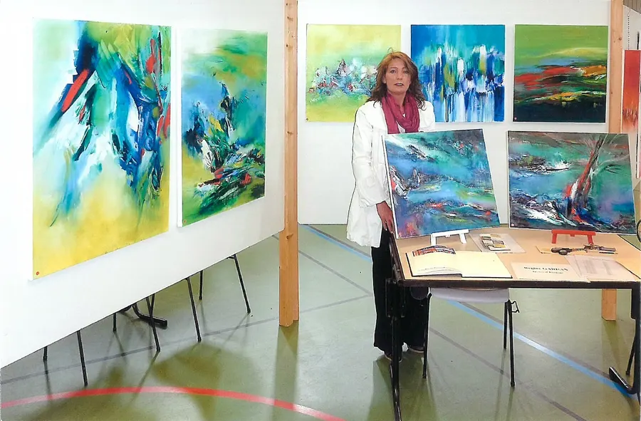 Régine Gardan à son exposition, entourée de ses tableaux abstraits aux couleurs vives