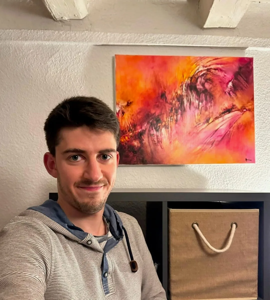 Lucas devant son tableau abstrait orange et rose de Régine Gardan, accroché dans son salon à Lyon